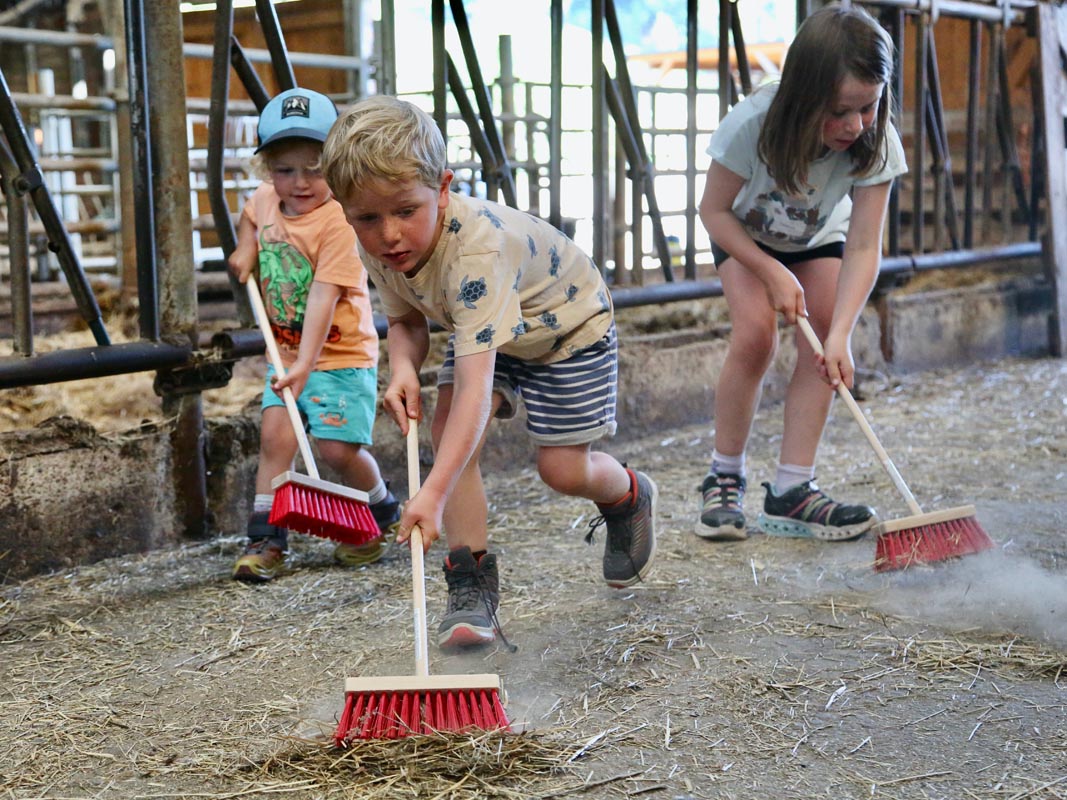 Drei Kinder kehren gemeinsam mit Besen den Stall des Tiggeshofs