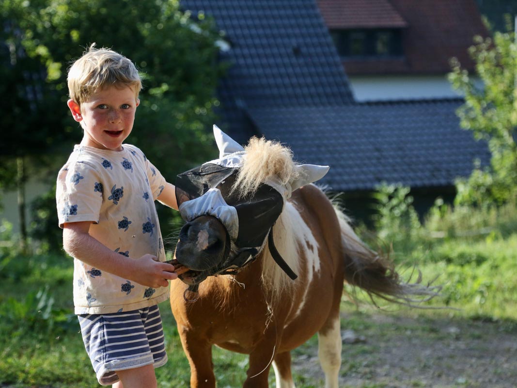 Kind steht neben einem Pony auf dem Hof des Tiggeshofs